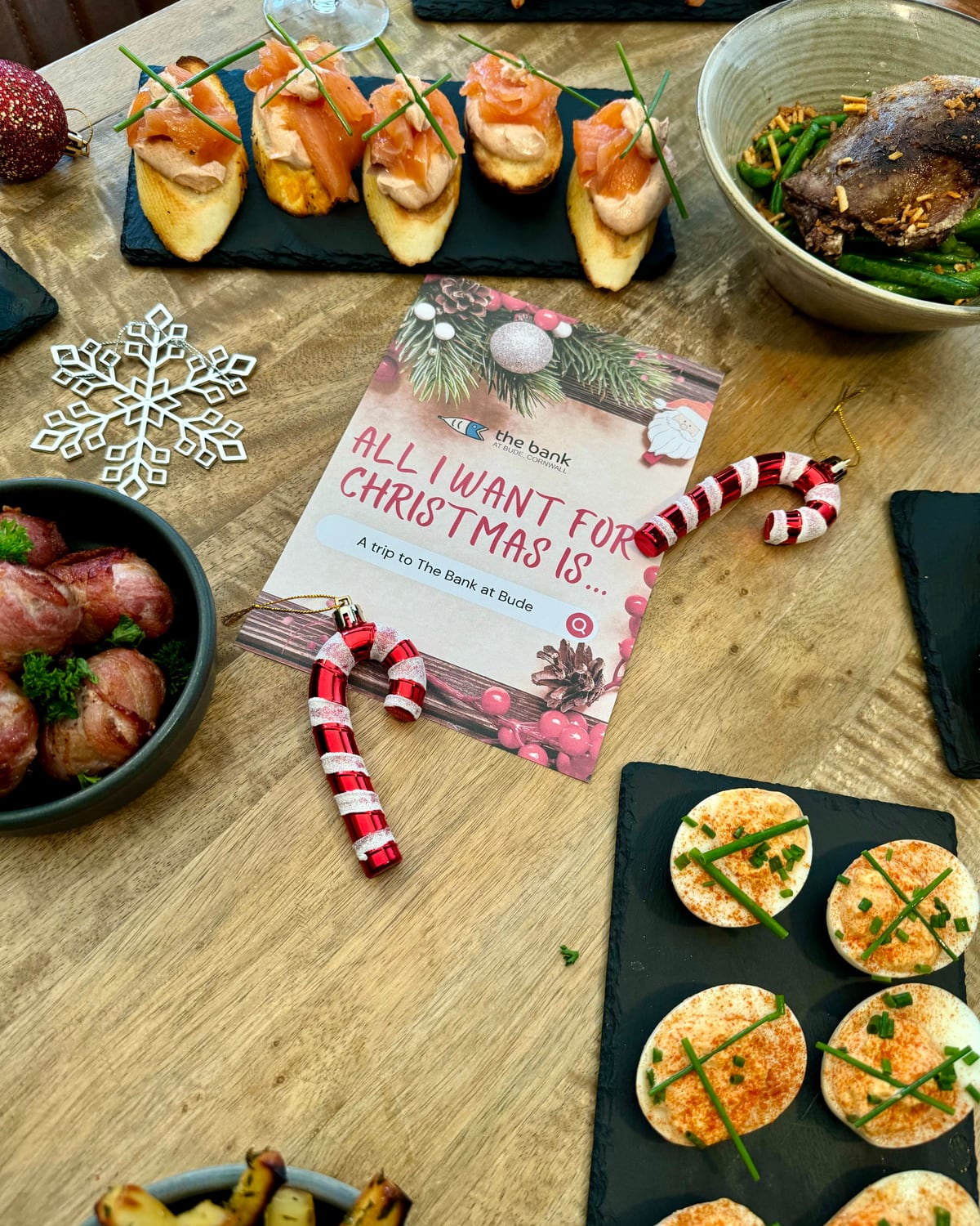 A festive “All I want for Christmas is a trip to The Bank at Bude” card among canapés and decorations