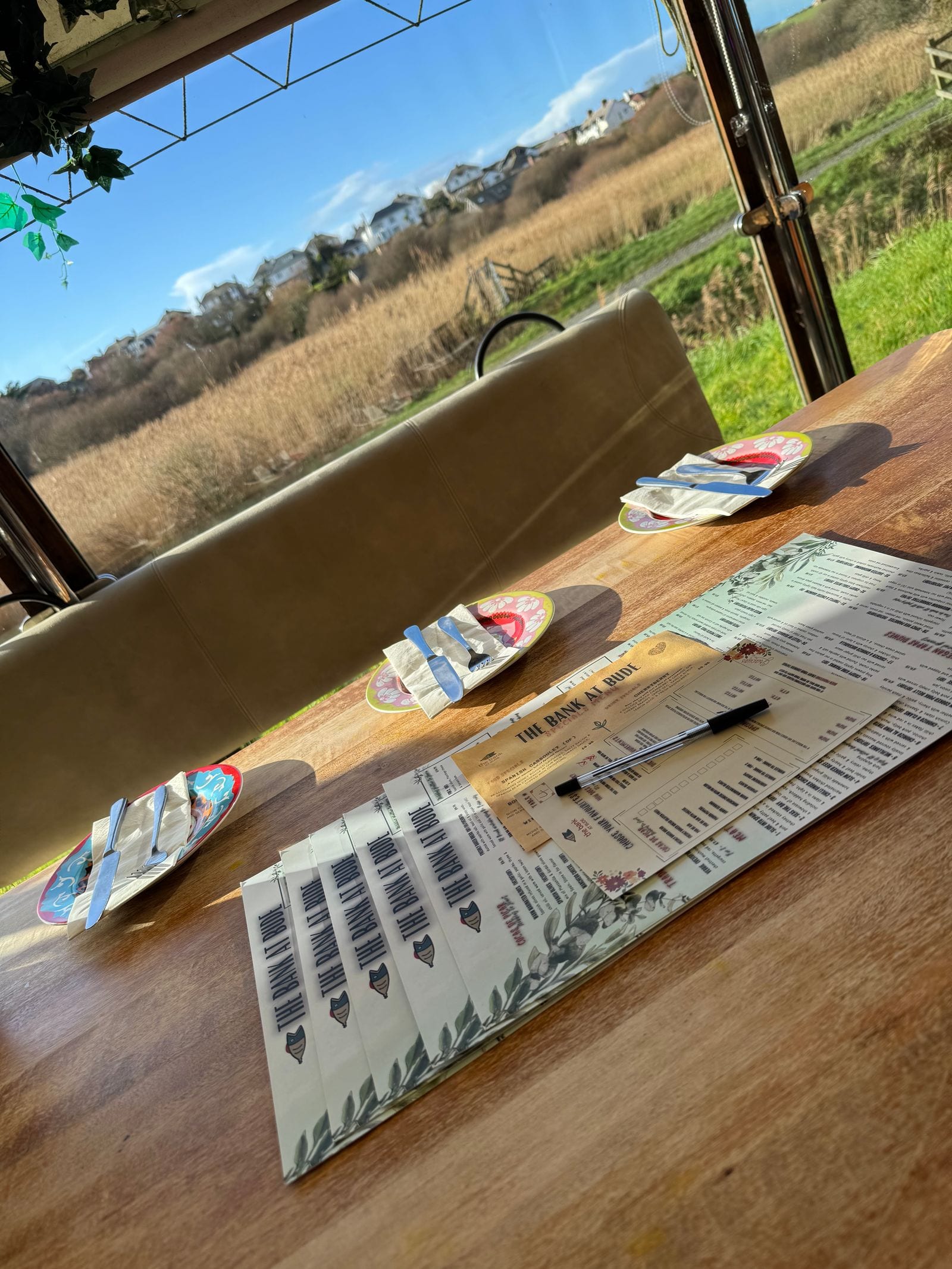 A table laid with menus inside The Bank at Bude, looking out over the River Neet marsh towards Bude